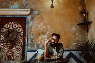 Portrait of young man using phone while sitting on table