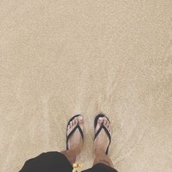 Low section of man standing on sand at beach