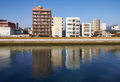 Reflection of buildings in river against clear blue sky