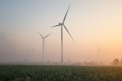Wind turbines on field against sky during sunset
