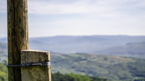 Close-up of wooden post on landscape against sky