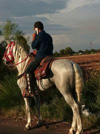 Man riding horse while talking on cellphone against sky