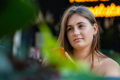 Close-up of young woman holding smart phone standing outdoors