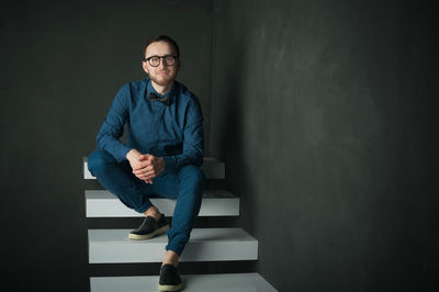 Portrait of man sitting on steps against black background