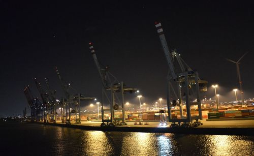 Illuminated commercial dock by sea against clear sky at night