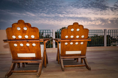 Empty chairs and tables against sky at sunset