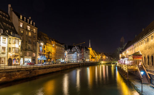 Illuminated buildings by river against sky at night