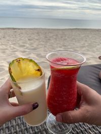 Cropped image of hand holding drink at beach against sky