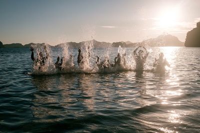 Water splashing in sea against sky during sunset