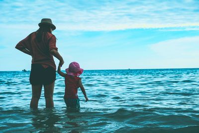 Rear view of mother and daughter on sea against sky