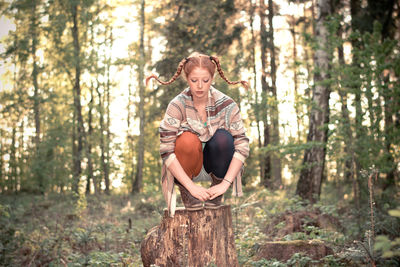 Full length of woman crouching on tree stump in forest