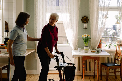 Side view of female healthcare worker supporting elderly woman with rollator in nursing home
