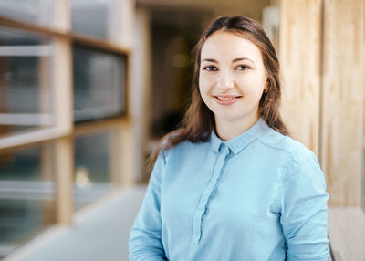 Portrait of happy young businesswoman standing at office corridor