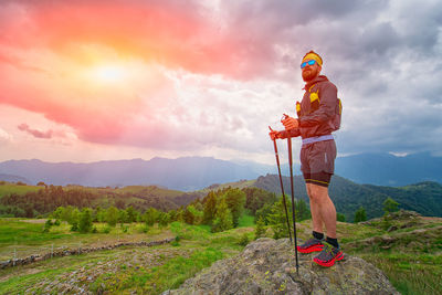 Rear view of man standing on mountain against sky during sunset