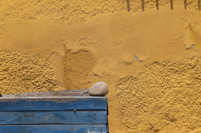 Close-up of small rock on a blue wooden box against yellow wall