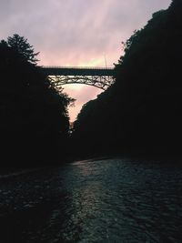 Silhouette of bridge over river at sunset