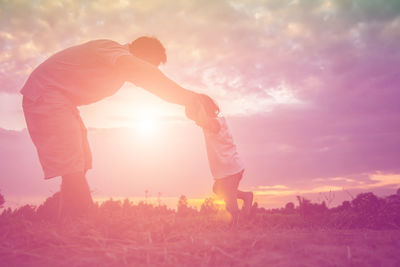 Rear view of friends standing on field against sky during sunset