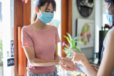Young women wearing mask sanitizing hands at home