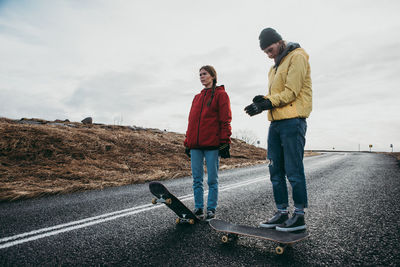 Full length of young man and woman skateboarding on road against landscape