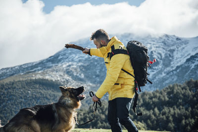 Young man with yellow jacket and backpack plays with german shepherd d