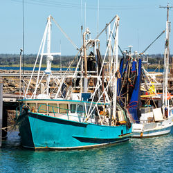 Fishing boats moored at harbor against clear blue sky