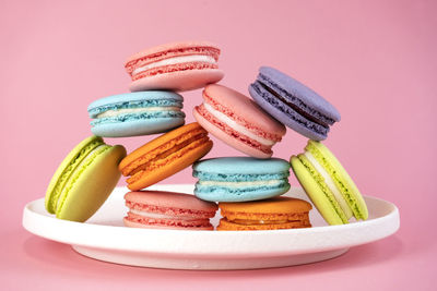 Delicious colorful french macaroons on white plate. pink background.