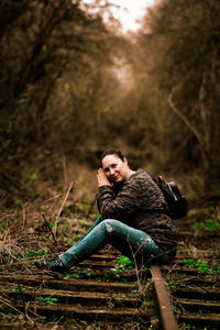 Portrait of young woman sitting on land in forest