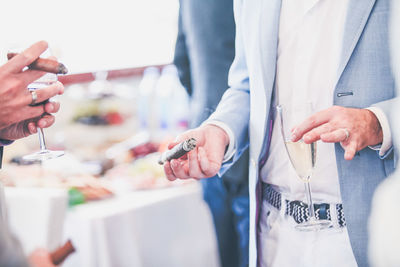 Cropped image of people holding cigar wand wineglass