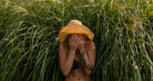 Young woman covering face while standing against plants