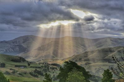 Idyllic shot of sunbeam over landscape against cloudy sky