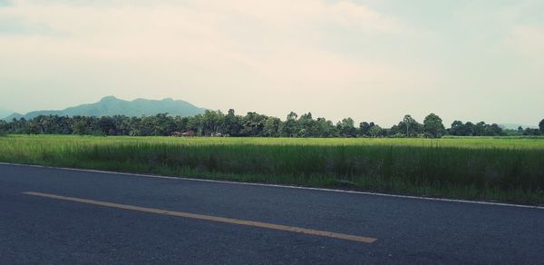 Scenic view of road by field against sky