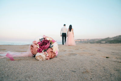 Close-up of bouquet on sand with couple in background