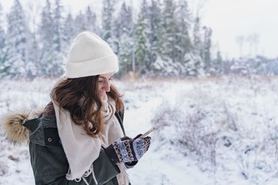 Young woman using phone while standing on snow covered landscape