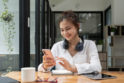 Young woman using mobile phone while sitting on table