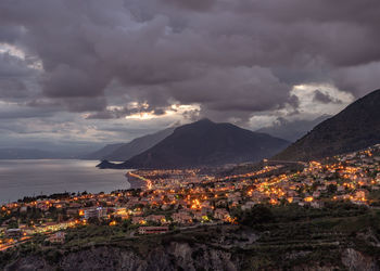 Aerial view of illuminated cityscape and mountains against storm clouds