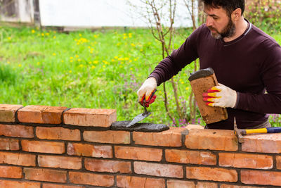 Side view of young man sitting on retaining wall