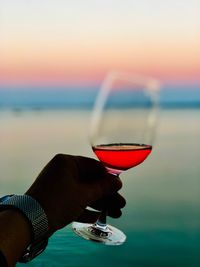 Close-up of hand holding wine glass against sunset