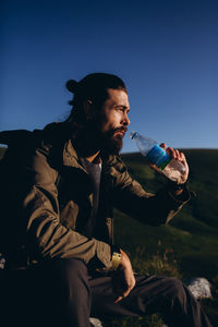 Man drinking water from bottle while sitting against sky