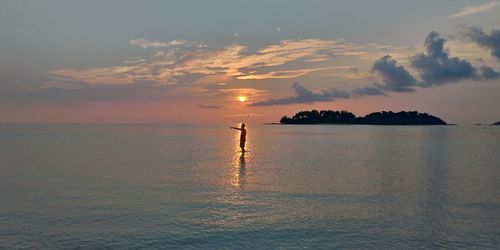 Man standing in sea against sky during sunset