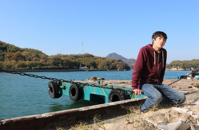 Man sitting by boat against clear blue sky