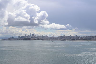 View of city at waterfront against cloudy sky