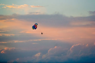 Low angle view of people paragliding against sky during sunset