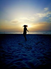 Silhouette man standing in sea against sky during sunset