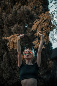 Young woman holding plant while standing against trees