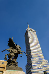 Low angle view of torre latinoamericana by statue against clear blue sky in city