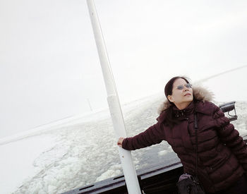 Woman in warm clothing traveling in boat on frozen sea during foggy weather