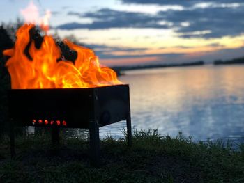 Bonfire by lake against sky during sunset