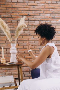 Side view of young black woman sitting against brick wall