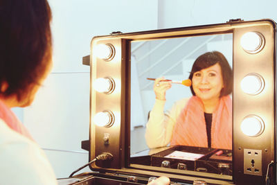 Close-up of woman doing make up in front of vanity mirror 