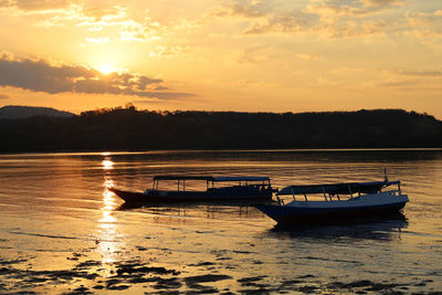 Fishing boat in lake against sky during sunset